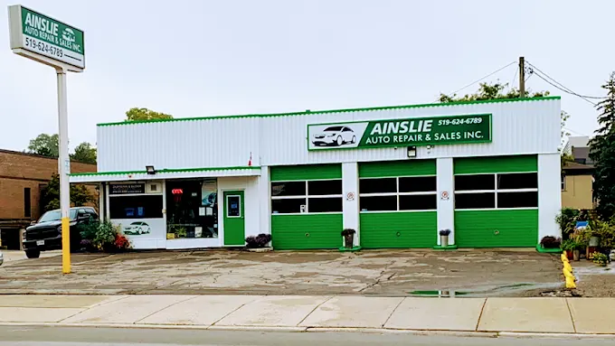 The front of the shop on Water Street: white siding, the green Ainslie sign and three green bay doors, with the pylon sign at the road.